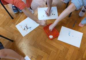 przedszkolaki próbują malować pędzelkiem trzymanym przez palce nogi