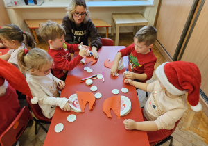 mama siedzi wśród dzieci i pomaga dzieciom wykonać pracę