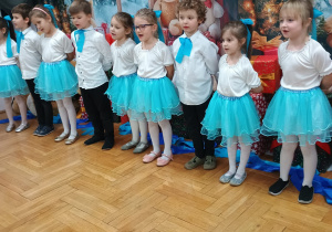 przedszkolaki stoją i śpiewają stojąc w półkolu