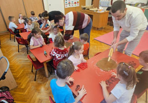 rodzice wałkują ciasto na pierniczki na stolikch, przy których siedzą dzieci