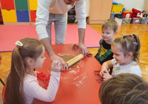 tata wałkuje ciasto na pierniczki na stoliku, przy którym siedzą dzieci