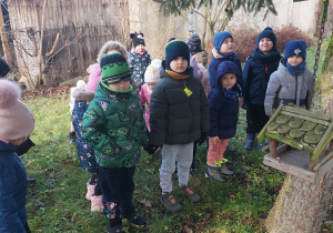 dzieci stojąw ogrodzie przedszkolnym przy karmniku