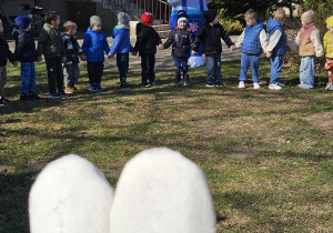 Zając Wielkanocny zbliża się do dzieci stojąych w kole w ogrodzie przedszkolnym