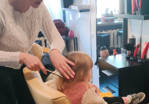 fryzjerka czesze dziewczynkę, która siedzi na fotelu przed lustrem