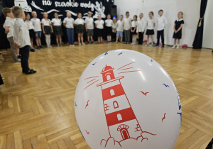 starszaki stoją w półkolu i śpiewają na tle balonu z czerwoną latarnią