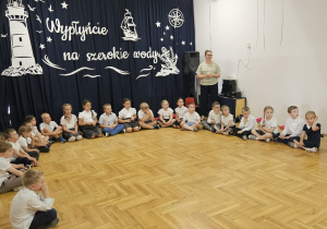 dzieci siedzą w półkolu a przy nich stoi nauczycielka