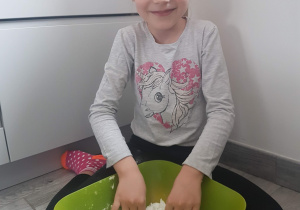 dziewczynka siedzi w kuchni , na podłodze i miesza makę z solą