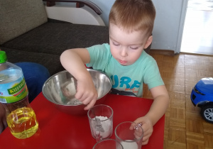 chłopiec wsypuje łyżką mąkę ze szklanki do miski a obok stoi olej