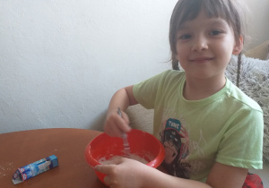 dziewczynka w warkoczach siedzi i przy stoliku miesza składniki na ciasto