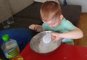 chłopiec wlewa wodę ze szklanki do miski