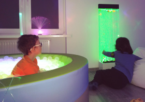 chłopiec siedzi w podświetlanym basenie z kulkami a drugi patrzy na podświetlane akwarium