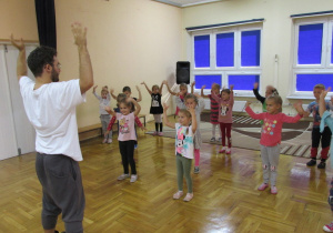 dzieci tańczą z instruktorem z rękami uniesionymi po bokach