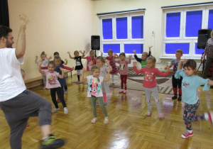 dzieci tańczą z instruktorem z rękami uniesionymi po bokach i jedną nogą