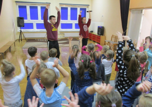 para tancerzy stoi przed dziećmi i pokazuje ruchy, które dzieci powtarzają