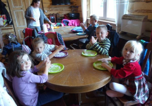 dzieci siedzą przy okrągłych, drewnianych stolikach na zielonych talerzykach zagniatają ciasto