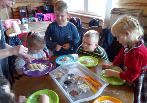 dzieci przy stoliku obsypują ciasto różnymi ziarenkami zbóż