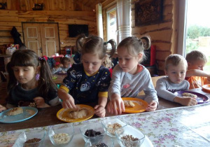 dzieci przy stoliku, na swoich talerzykach sypią na pieczywo ziarna