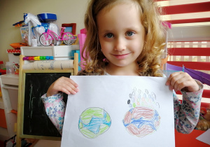 dziewczynka w kręconych włosach pokazuje swoja pracę; dwie kule ziemskie ładna i brzydką narysowane kredkami