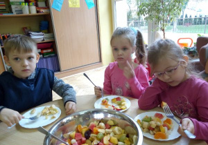 dzieci przy stoliku i jedzą sałatkę owocową z talerzyków