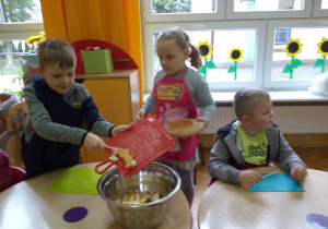 dzieci wsypują pokrojone owoce do dużej, srebrnej miski na środku stolika
