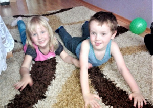 rodzeństwo leży na dywanie na brzuchu i robi "foczkę"
