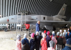 dzieci stoją w hangarze, w którym stoi samolot wojskowy
