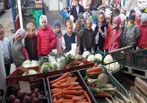 dzieci z panią stoją przed straganem na ryneczku z warzywami
