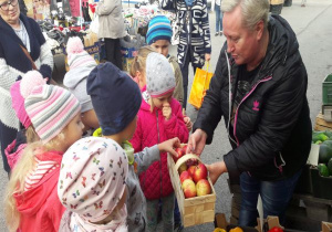 sprzedawczyni daje dzieciom koszyk z jabłkami
