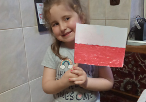 dziewczynka stoi i trzyma w rękach flagę wykonaną w domu