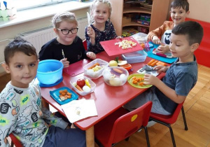 dzieci kroją warzywa przy prostokątnym stoliku