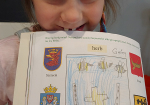 dziewczynka pokazuje narysowany kredkami, w książce herb miasta Zduńskiej Woli