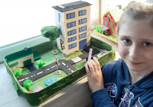 dziewczynka pokazuje makietę miasta z domami , ulicami i znakami drogowymi