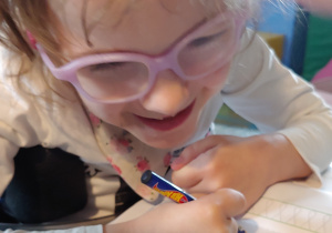 dziewczynka w okularach, uśmiecha się i pisze długopisem w książce