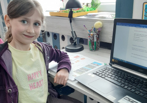 dziewczynka siedzi w swoim pokoju przy biurku, przed komputerem i książką