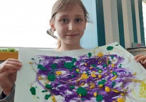 dziewczynka pokazuje prac plastyczną: kolorowe plamy fioletowe, niebieskie i żółte