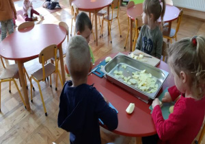 dzieci kroją jabłka i wrzucają do dużej metalowej blachy na środku stolika