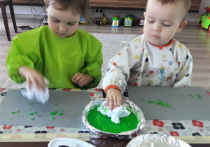 dzieci w domu, siedzą przy stole stemplują zmiętą chusteczką maczaną w zielonej farbie