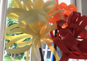 prac plastyczno- techniczna: dwa kwiaty zamocowane na patykach, wykonane z cienkich pasków kolorowego papieru żółtego i czerwonego