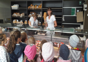 pani pokazuje chleb dzieciom, które stoją przed szklaną ladą