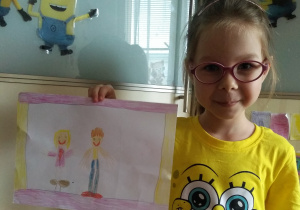 dziewczynka w okularach pokazuje swoja pracę z narysowana kredką swoją rodziną