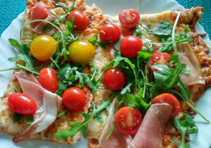 napis "ulubiony deser mamy" a pod nim talerz na niebieskim tle z pizzą z liściami rukoli, szynką i małymi pomidorkami