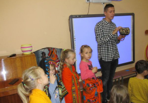 Mateusz pokazuje naczynie zdobione wzorami a dziewczynki stoją ubrane w regionalne chusty