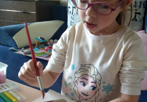 dziewczynka siedzi przy stole i maluje brązową farbą rolkę papieru