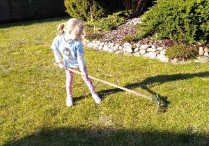 dziewczynka w ogrodzie grabi trawę
