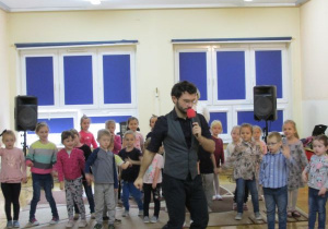 dzieci tańczą z prowadzącym, który trzyma mikrofon
