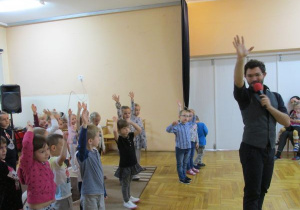 dzieci tańczą z prowadzącym i robią "słoneczko" jedna ręką w górze