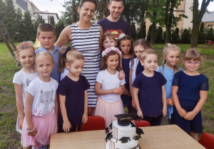 w ogrodzie stoją przy stole z tortem 6-latki z gr. VI z nauczycielką oraz tatą, który wykonał tort