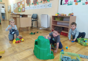 w sali chłopcy bawią się na podłodze zabawkami obok biurka nauczycielki