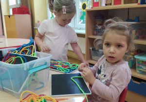 dwie dziewczynki bawią się sznurkami i układają je na tabliczkach na rzep
