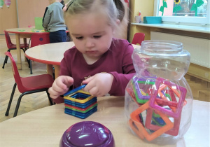 dziewczynka przy stoliku układa klocki magnetyczne w kształcie kwadratu jedne na drugim